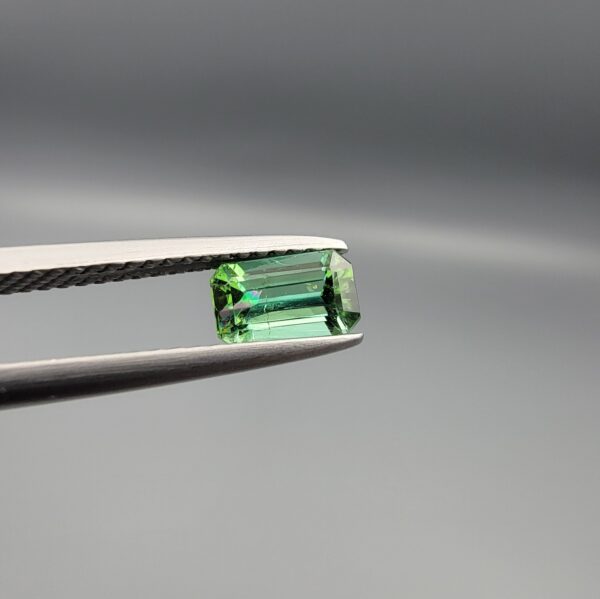 Studio close-up photographs showing the top and facet profile views of a 0.94 carat octagon cut natural blue tourmaline loose gemstone held in precision tweezers.