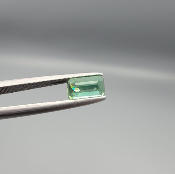 Studio close-up photographs showing the top and facet profile views of a 0.94 carat octagon cut natural blue tourmaline loose gemstone held in precision tweezers.