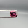 Studio close-up photographs showing the top table face, step-cut pavilion facets, and reverse profile views of a 3.17 carat cushion cut natural rhodolite garnet loose gemstone held in precision tweezers.