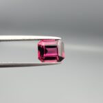 Studio close-up photographs showing the top table face, step-cut pavilion facets, and reverse profile views of a 3.17 carat cushion cut natural rhodolite garnet loose gemstone held in precision tweezers.