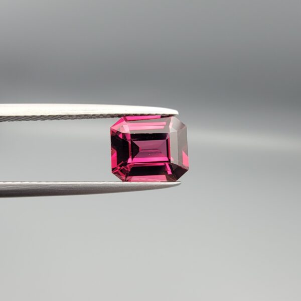 Studio close-up photographs showing the top table face, step-cut pavilion facets, and reverse profile views of a 3.17 carat cushion cut natural rhodolite garnet loose gemstone held in precision tweezers.