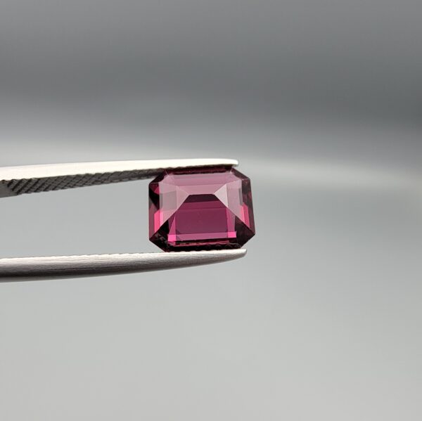 Studio close-up photographs showing the top table face, step-cut pavilion facets, and reverse profile views of a 3.17 carat cushion cut natural rhodolite garnet loose gemstone held in precision tweezers.