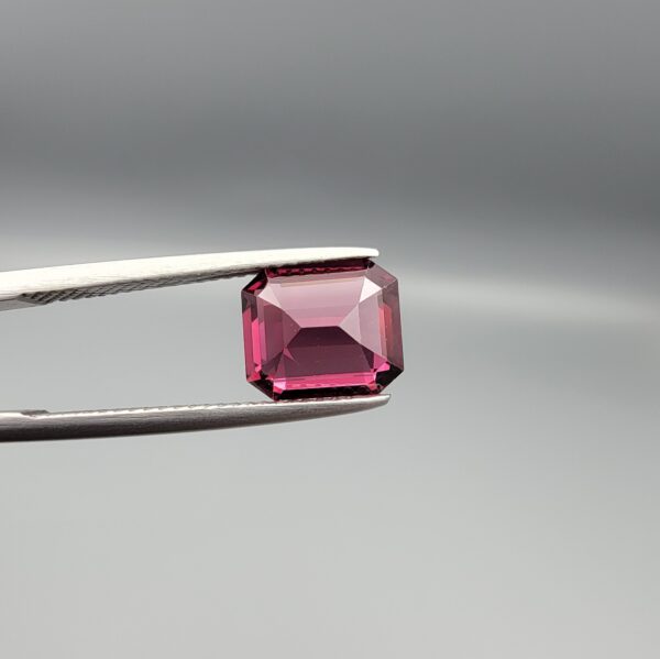 Studio close-up photographs showing the top table face, step-cut pavilion facets, and reverse profile views of a 3.17 carat cushion cut natural rhodolite garnet loose gemstone held in precision tweezers.