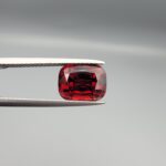 Studio close-up photographs showing the top table face, step-cut pavilion facets, and reverse profile views of a 4.55 carat cushion cut natural almandine garnet loose gemstone held in precision tweezers.