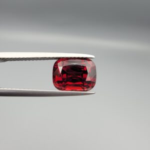 Studio close-up photographs showing the top table face, step-cut pavilion facets, and reverse profile views of a 4.55 carat cushion cut natural almandine garnet loose gemstone held in precision tweezers.