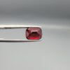 Studio close-up photographs showing the top table face, step-cut pavilion facets, and reverse profile views of a 4.55 carat cushion cut natural almandine garnet loose gemstone held in precision tweezers.