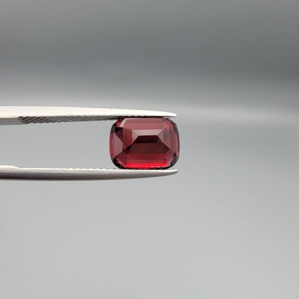 Studio close-up photographs showing the top table face, step-cut pavilion facets, and reverse profile views of a 4.55 carat cushion cut natural almandine garnet loose gemstone held in precision tweezers.