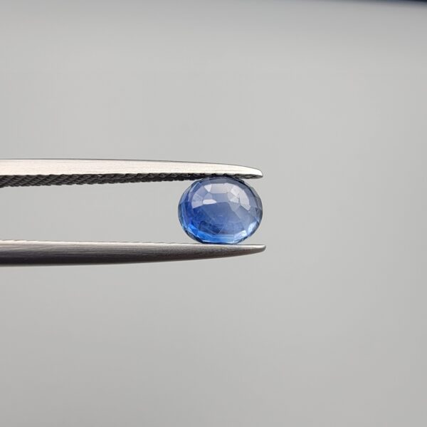 Studio close-up photographs showing the top table and side facet profile views of a 1.19 carat oval cut natural blue sapphire loose gemstone held in precision tweezers.