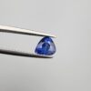 Studio close-up photographs showing the top table and facet profile views of a 1.26 carat pear cut natural blue sapphire loose gemstone held in precision tweezers.