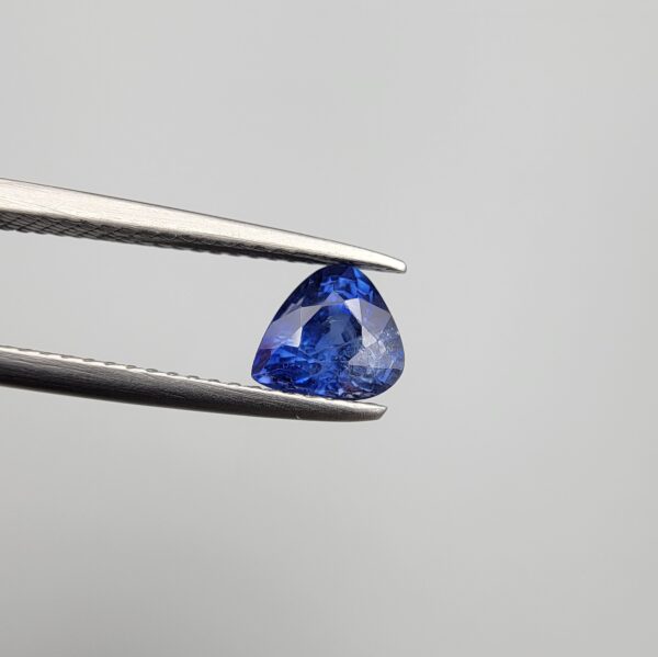 Studio close-up photographs showing the top table and facet profile views of a 1.26 carat pear cut natural blue sapphire loose gemstone held in precision tweezers.