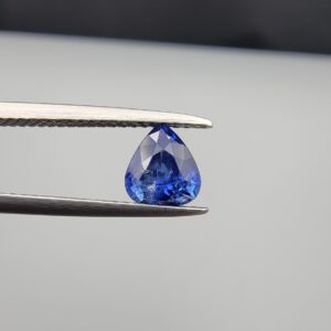 Studio close-up photographs showing the top table and facet profile views of a 1.26 carat pear cut natural blue sapphire loose gemstone held in precision tweezers.