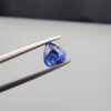 Studio close-up photographs showing the top table and facet profile views of a 1.26 carat pear cut natural blue sapphire loose gemstone held in precision tweezers.