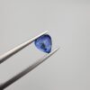 Studio close-up photographs showing the top table and facet profile views of a 1.26 carat pear cut natural blue sapphire loose gemstone held in precision tweezers.