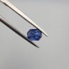 Studio close-up photographs showing the top table and step-cut profile views of a 1.00 carat octagon cut natural blue sapphire loose gemstone held in precision tweezers.