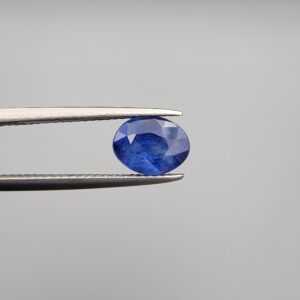 Studio close-up photographs showing the top table and side facet profile views of a 2.44 carat oval cut natural blue sapphire loose gemstone held in precision tweezers.