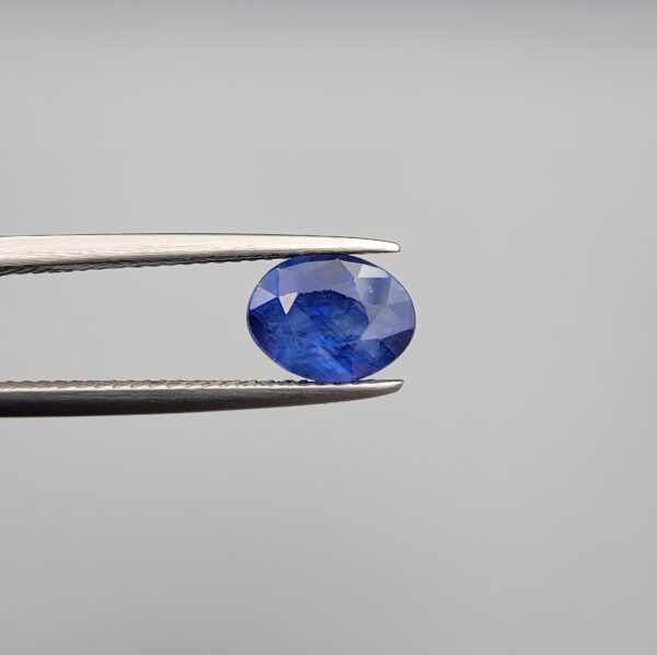 Studio close-up photographs showing the top table and side facet profile views of a 2.44 carat oval cut natural blue sapphire loose gemstone held in precision tweezers.
