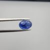 Studio close-up photographs showing the top table and side facet profile views of a 2.44 carat oval cut natural blue sapphire loose gemstone held in precision tweezers.