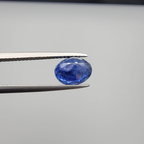 Studio close-up photographs showing the top table and side facet profile views of a 2.44 carat oval cut natural blue sapphire loose gemstone held in precision tweezers.