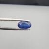 Studio close-up photographs showing the top table and side facet profile views of a 2.65 carat oval cut natural blue sapphire loose gemstone held in precision tweezers.