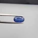 Studio close-up photographs showing the top table and side facet profile views of a 2.65 carat oval cut natural blue sapphire loose gemstone held in precision tweezers.