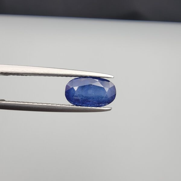 Studio close-up photographs showing the top table and side facet profile views of a 2.65 carat oval cut natural blue sapphire loose gemstone held in precision tweezers.