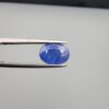 Studio close-up photographs showing the top table and side facet profile views of a 3.64 carat oval cut natural blue sapphire loose gemstone held in precision tweezers.