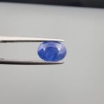 Studio close-up photographs showing the top table and side facet profile views of a 3.64 carat oval cut natural blue sapphire loose gemstone held in precision tweezers.