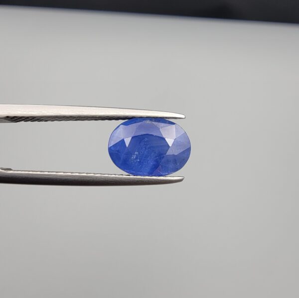 Studio close-up photographs showing the top table and side facet profile views of a 3.64 carat oval cut natural blue sapphire loose gemstone held in precision tweezers.