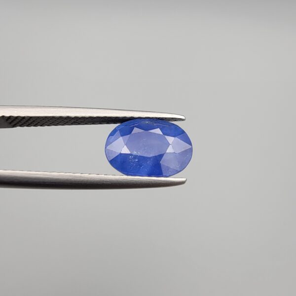 Studio close-up photographs showing the top table and side facet profile views of a 3.64 carat oval cut natural blue sapphire loose gemstone held in precision tweezers.