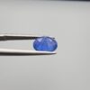 Studio close-up photographs showing the top table and side facet profile views of a 3.64 carat oval cut natural blue sapphire loose gemstone held in precision tweezers.