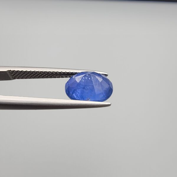 Studio close-up photographs showing the top table and side facet profile views of a 3.64 carat oval cut natural blue sapphire loose gemstone held in precision tweezers.