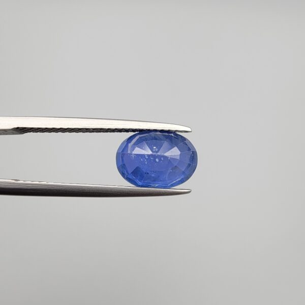 Studio close-up photographs showing the top table and side facet profile views of a 3.64 carat oval cut natural blue sapphire loose gemstone held in precision tweezers.