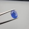 Studio close-up photographs showing the top table and side facet profile views of a 3.64 carat oval cut natural blue sapphire loose gemstone held in precision tweezers.
