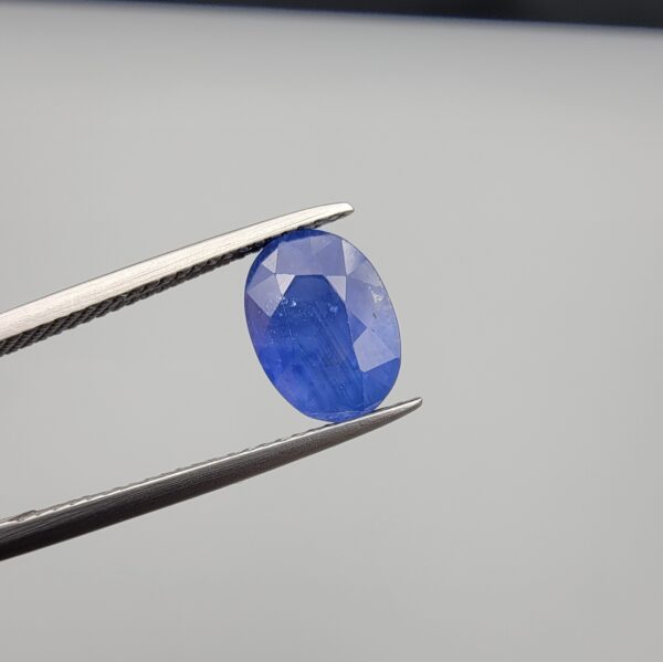 Studio close-up photographs showing the top table and side facet profile views of a 3.64 carat oval cut natural blue sapphire loose gemstone held in precision tweezers.