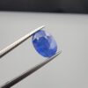 Studio close-up photographs showing the top table and side facet profile views of a 3.64 carat oval cut natural blue sapphire loose gemstone held in precision tweezers.