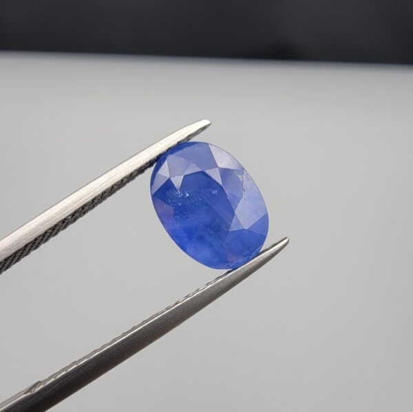 Studio close-up photographs showing the top table and side facet profile views of a 3.64 carat oval cut natural blue sapphire loose gemstone held in precision tweezers.