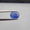Studio close-up photographs showing the top table and side facet profile views of a 2.17 carat oval cut natural blue sapphire loose gemstone held in precision tweezers.