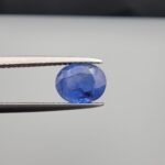 Studio close-up photographs showing the top table and side facet profile views of a 2.17 carat oval cut natural blue sapphire loose gemstone held in precision tweezers.