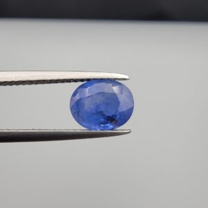 Studio close-up photographs showing the top table and side facet profile views of a 2.17 carat oval cut natural blue sapphire loose gemstone held in precision tweezers.
