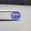 Studio close-up photographs showing the top table and side facet profile views of a 2.17 carat oval cut natural blue sapphire loose gemstone held in precision tweezers.