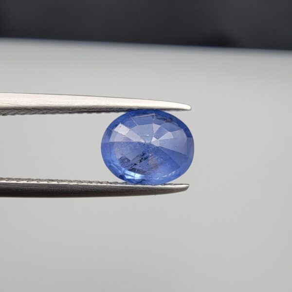 Studio close-up photographs showing the top table and side facet profile views of a 2.17 carat oval cut natural blue sapphire loose gemstone held in precision tweezers.