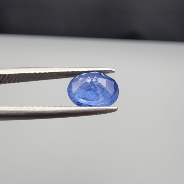 Studio close-up photographs showing the top table and side facet profile views of a 2.17 carat oval cut natural blue sapphire loose gemstone held in precision tweezers.