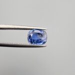 Studio close-up photographs showing the top table and side facet profile views of a 1.97 carat cushion cut natural blue sapphire loose gemstone held in precision tweezers.