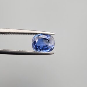 Studio close-up photographs showing the top table and side facet profile views of a 1.97 carat cushion cut natural blue sapphire loose gemstone held in precision tweezers.