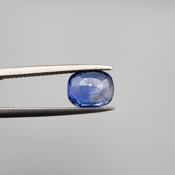 Studio close-up photographs showing the top table and side facet profile views of a 1.97 carat cushion cut natural blue sapphire loose gemstone held in precision tweezers.