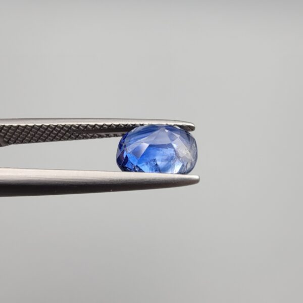 Studio close-up photographs showing the top table and side facet profile views of a 1.97 carat cushion cut natural blue sapphire loose gemstone held in precision tweezers.