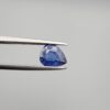 Studio close-up photographs showing the top table view with internal inclusions and reverse facet profile of a 1.41 carat pear cut natural blue sapphire loose gemstone held in precision tweezers.