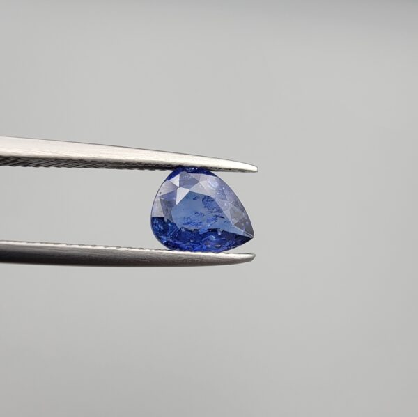 Studio close-up photographs showing the top table view with internal inclusions and reverse facet profile of a 1.41 carat pear cut natural blue sapphire loose gemstone held in precision tweezers.
