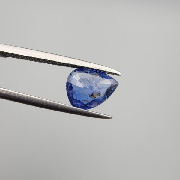 Studio close-up photographs showing the top table view with internal inclusions and reverse facet profile of a 1.41 carat pear cut natural blue sapphire loose gemstone held in precision tweezers.