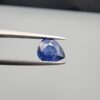 Studio close-up photographs showing the top table view with internal inclusions and reverse facet profile of a 1.41 carat pear cut natural blue sapphire loose gemstone held in precision tweezers.